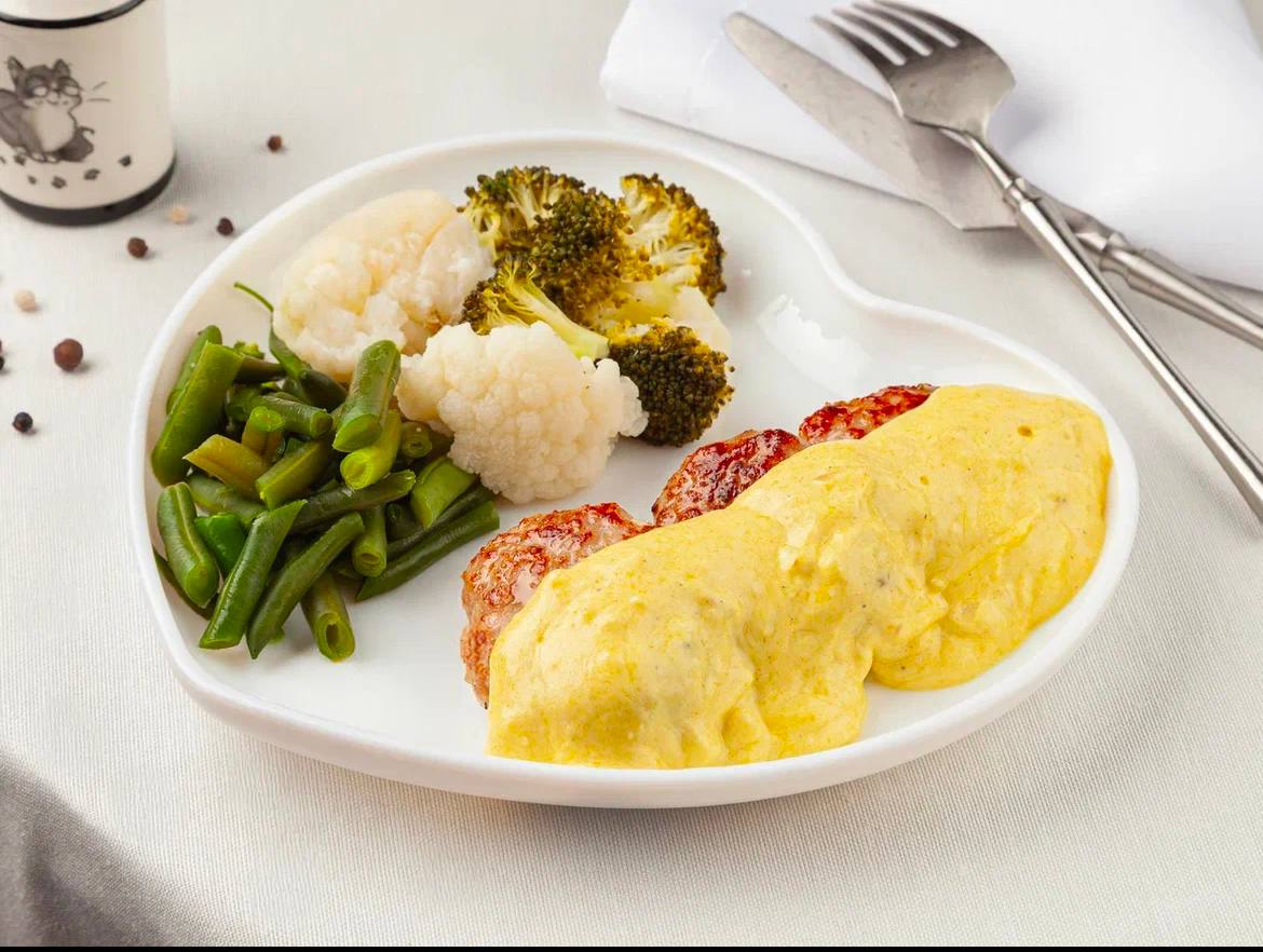 Original restaurant food photo with pale table, white plate, vegetables, and cutlets under yellow sauce