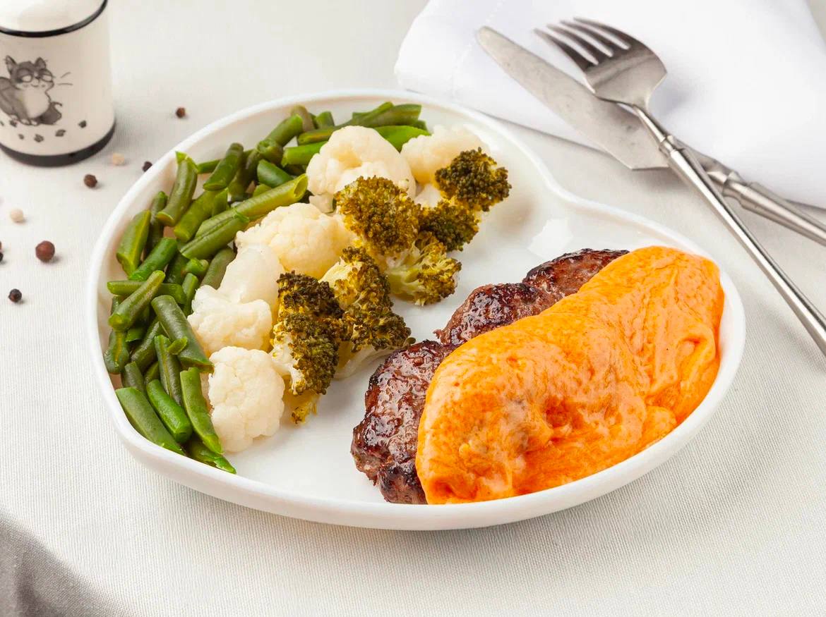 Original restaurant food photo with oval white plate, vegetables, and cutlets under orange sauce