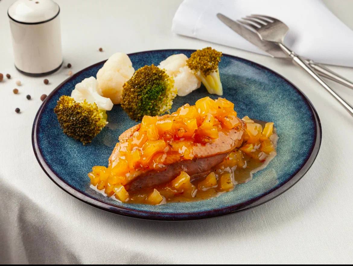 Original restaurant food photo with duck, orange sauce, cauliflower, and broccoli on a blue plate