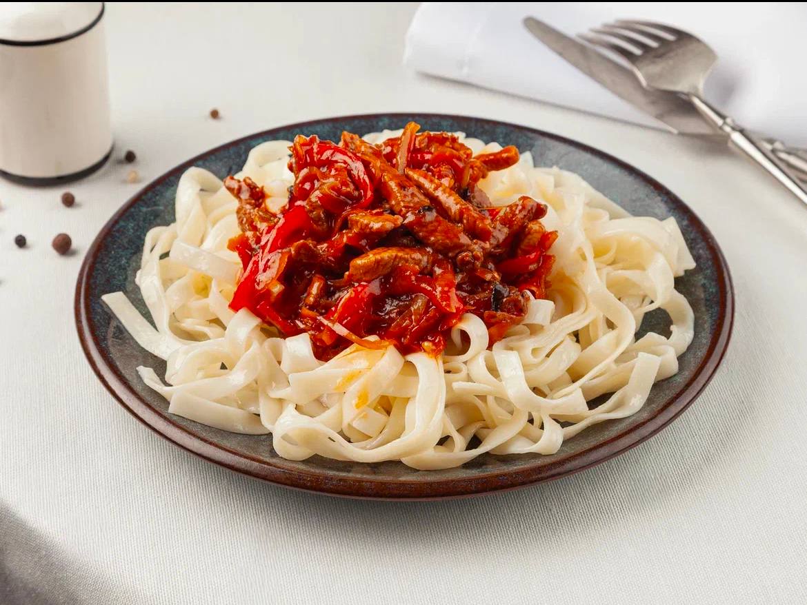 Original restaurant food photo with noodles and red sauce on a dark plate